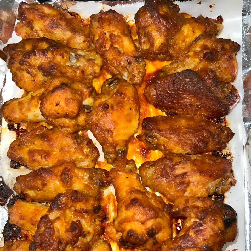 Close-up of a pan filled with golden-brown, saucy chicken wings from Sunnyside Pizza.
