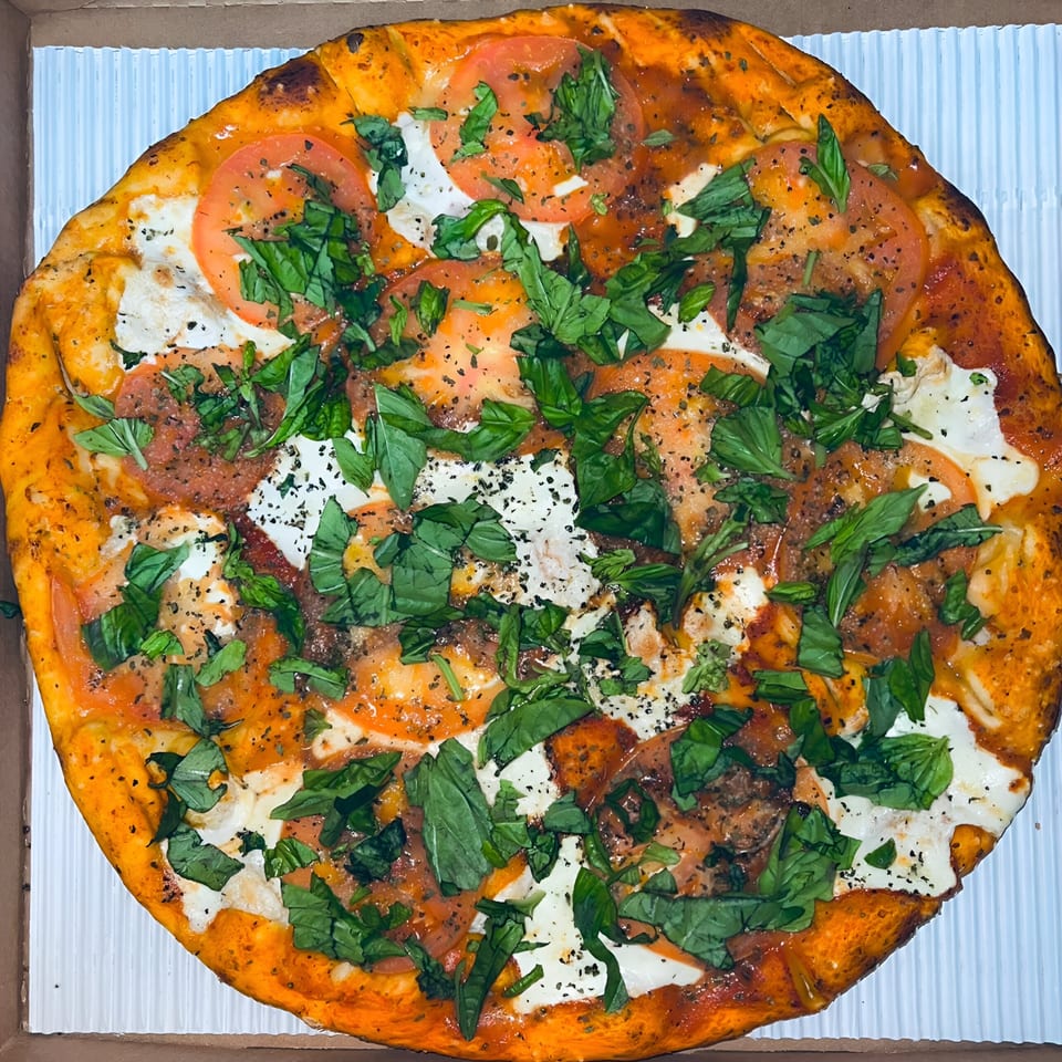 A Sunnyside Pizza Margherita pizza with fresh basil, sliced tomatoes, and mozzarella cheese.