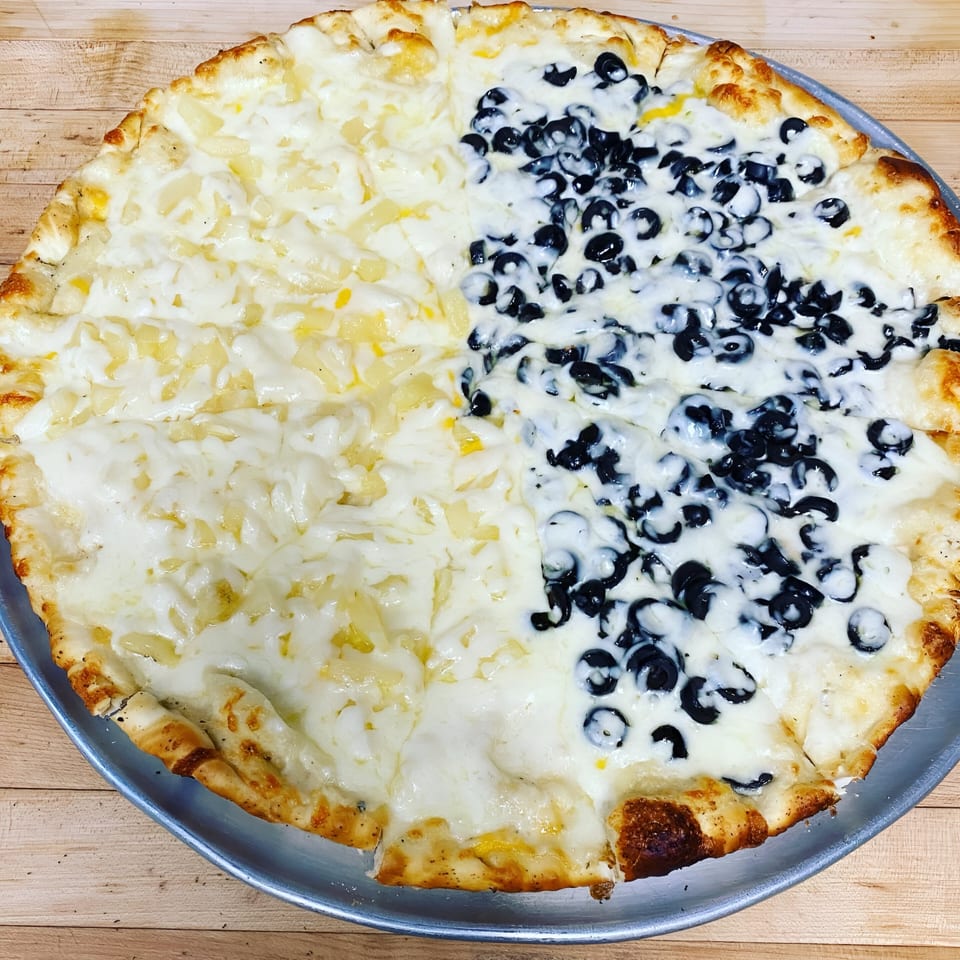 A Sunnyside Pizza with half pineapple and half black olives on a white sauce base.