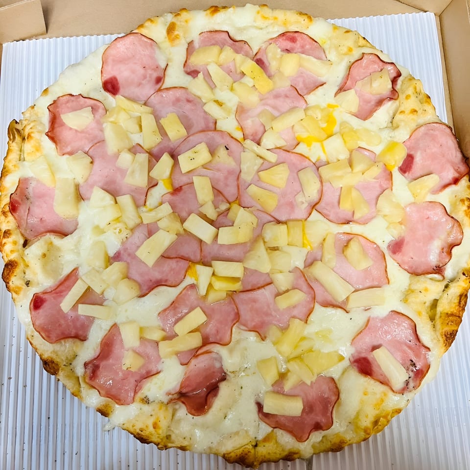 A whole Sunnyside Pizza with ham and pineapple toppings in a cardboard box.
